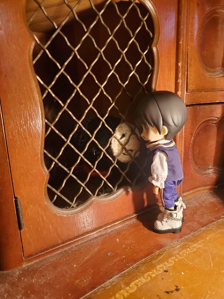 Martyn (nendoroid doll) leaning in as if to whisper or kiss Dollmaker (crochet critter), who is inside the bars of some sort of cell. 