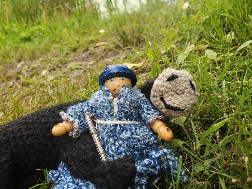 A wood doll in crochet dress and a crochet long doll cuddling on the grass