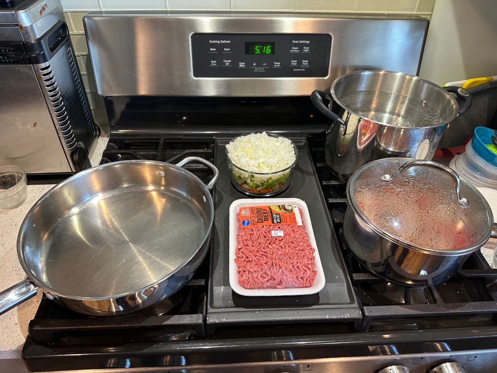 Pots and pans on a gas stove with bolognese ingredients mis en place