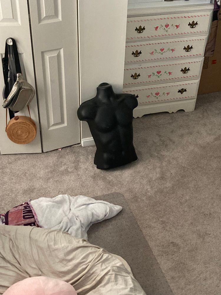 Photo of a black mannequin torso sitting propped up against a wall