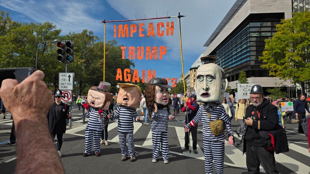 Paper mache heads of Trump, Stephen Miller, JD Vance, and Kristi Noem in prisoner outfits