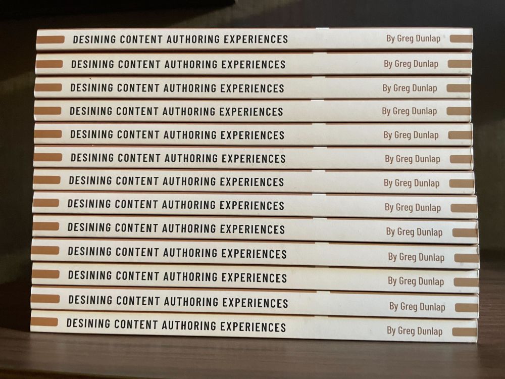A stack of 13 copies of the book Designing Content Authoring Experiences, stacked with the spines showing. The word "Designing" is accidentally spelled "Desining" because apparently 5 people reviewing the proofs wasn't enough.
