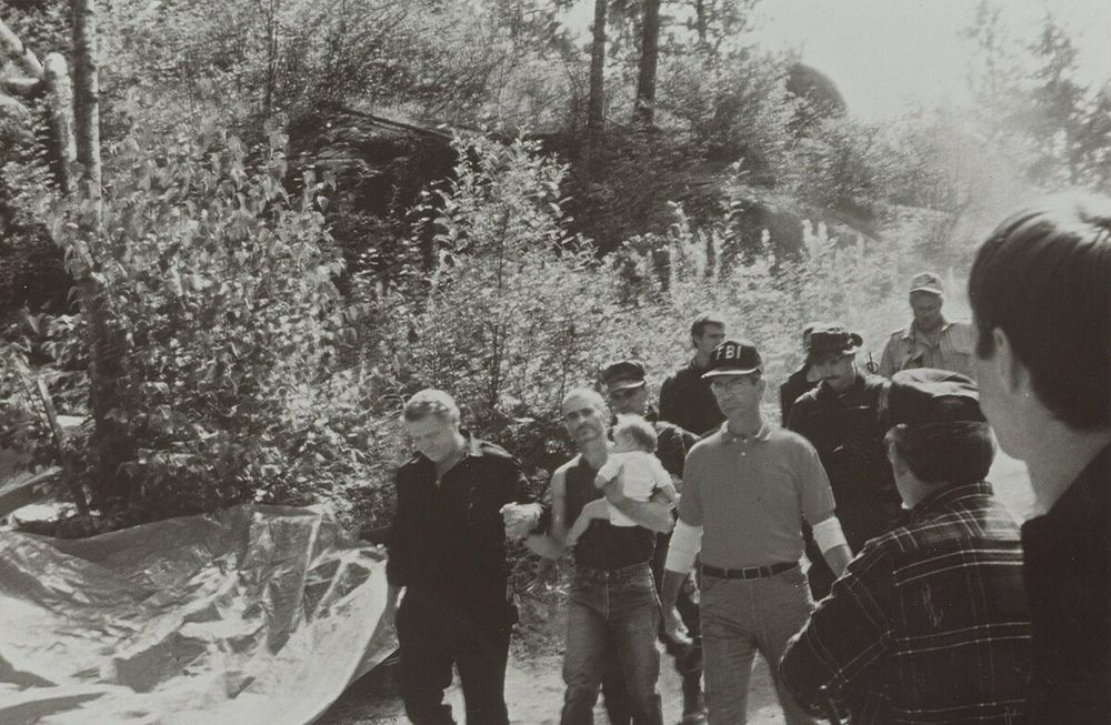 The surrender of Randy Weaver, who was Ashli Babbitt before Ashli Babbitt. In a black and white photo, Weaver is holding his infant daughter and flanked by an FBI agent and aⁿ Idaho state trooper whom he appears to be holding hands with, though maybe they’re cuffed to each other. They’re all wearing jeans, and there’s some uniformed officers behind them. There are two people in the foreground, both civilians, one of them in his teens. The FBI agent is arresting a literal terrorist with what appears to be a cell phone on his belt, and a button-down, not a bunch of body armor. 

Weaver sold automatic rifles to Nazis, and also a federal agent. He was small fry, but he got most of his family killed by entering a standoff with the Feds—he told his middle school aged sons to fire on federal officers. For whatever reason (president was a democrat/they love Nazis), republicans thought that this was egregious government overreach, something they couldn’t claim about the idiot in Oregon because we all saw the video of him pointing a gun at cops, and heard the audio clearly. This was impossible for Babbitt because she was surrounded by a bunch of other screaming terrorists, allowing them to create their own fantastic narrative. 
.