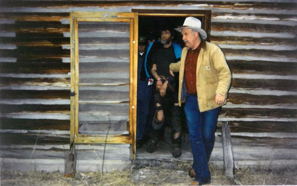 Ted Kaczynski, the Unabomber, being led out of his cabin by an FBI agent who looks like a rancher. No tactical gear, just a cowboy hat, and jeans. 
.