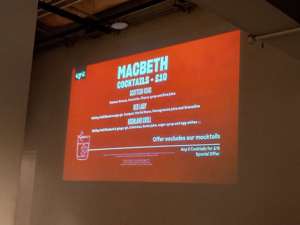 Picture of projection on a wall showing a cocktail menu, reads:
Macbeth cocktails £10
Scottish King: Famous Grouse, Amaretto, cherry syrup and lime juice
Red Lady: Whitley Neill blood orange gin, Campari, Martini Rosso, pomegranate juice and Grenadine
Highland Chill: Whitley Neill rhubarb and ginger gin, Cointreau, lemon juice, sugar syruo and egg whites