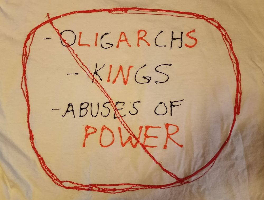 A home made T shirt with "oligarchs", "kings", and "abuses of power" in a red circle with a slash. Within the black text, some letters are orange. These read "liars in power". No more of this, please.