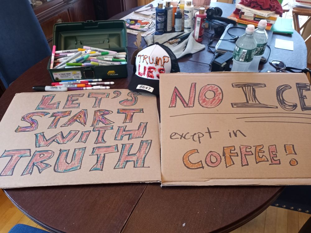 Two cardboard signs. One reads "Let's start with truth" and the other says "No ICE except in coffee". There is a baseball hat reading "Trump lies 8647"