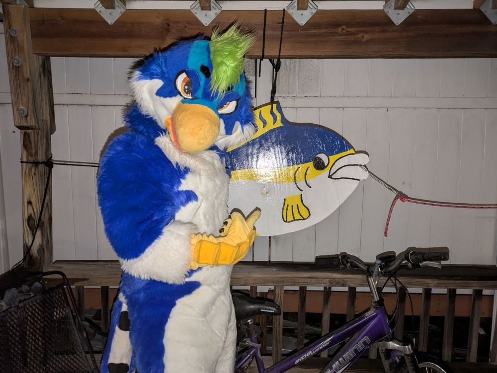Bird fursuit pointing at a fish sculpture 
