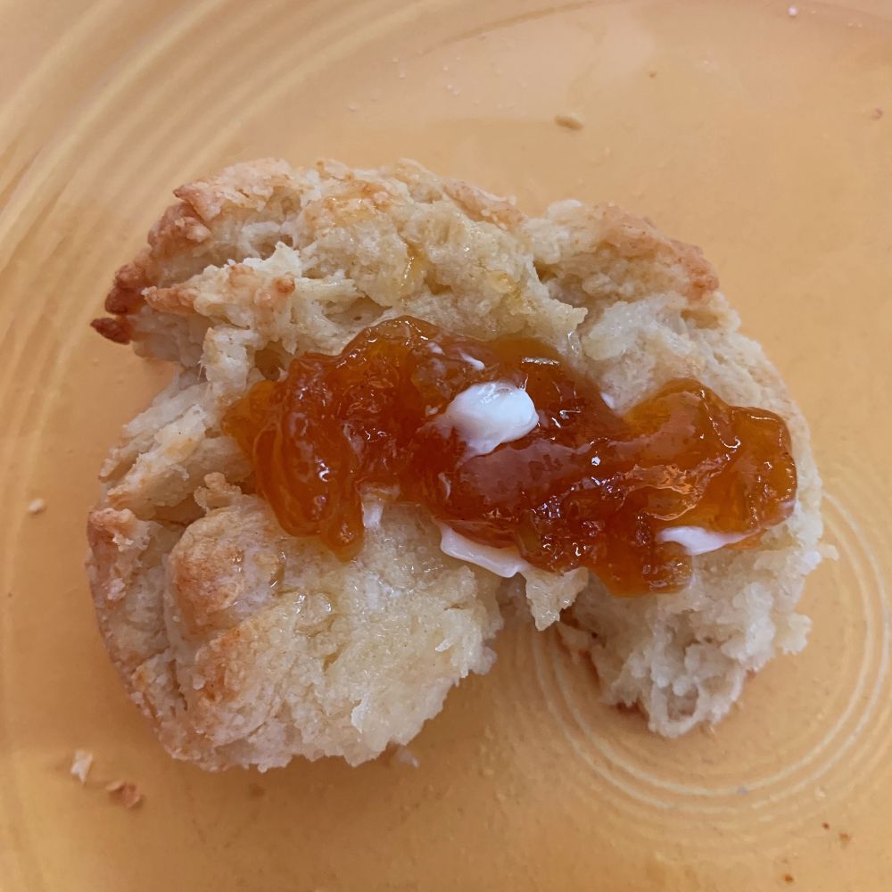 Half of a drop biscuit with butter and apricot preserves, served on a yellow plate.