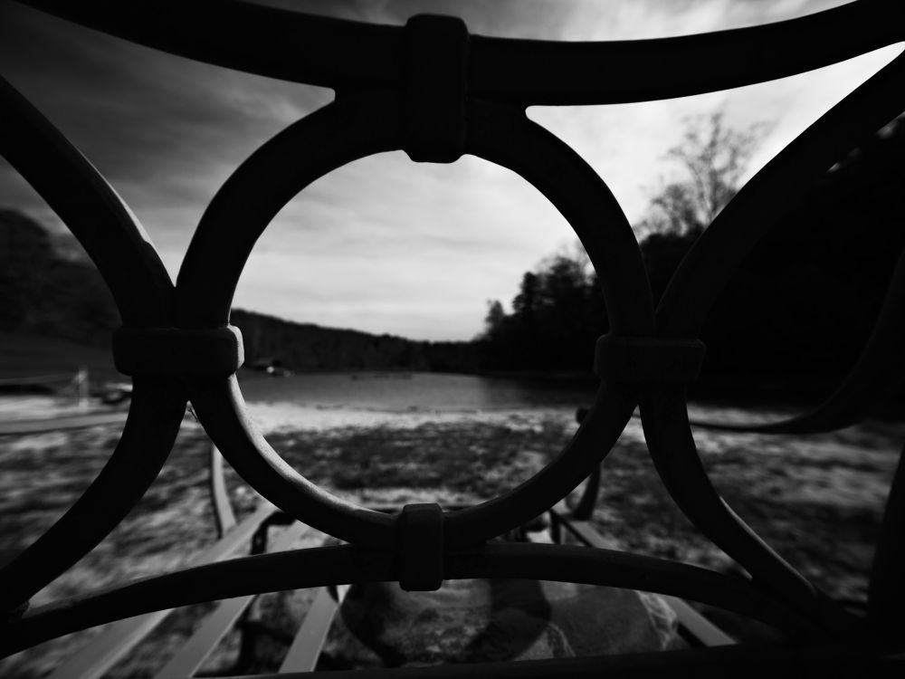 Pond and beach viewed through the porthole-shaped back of a lounge chair.