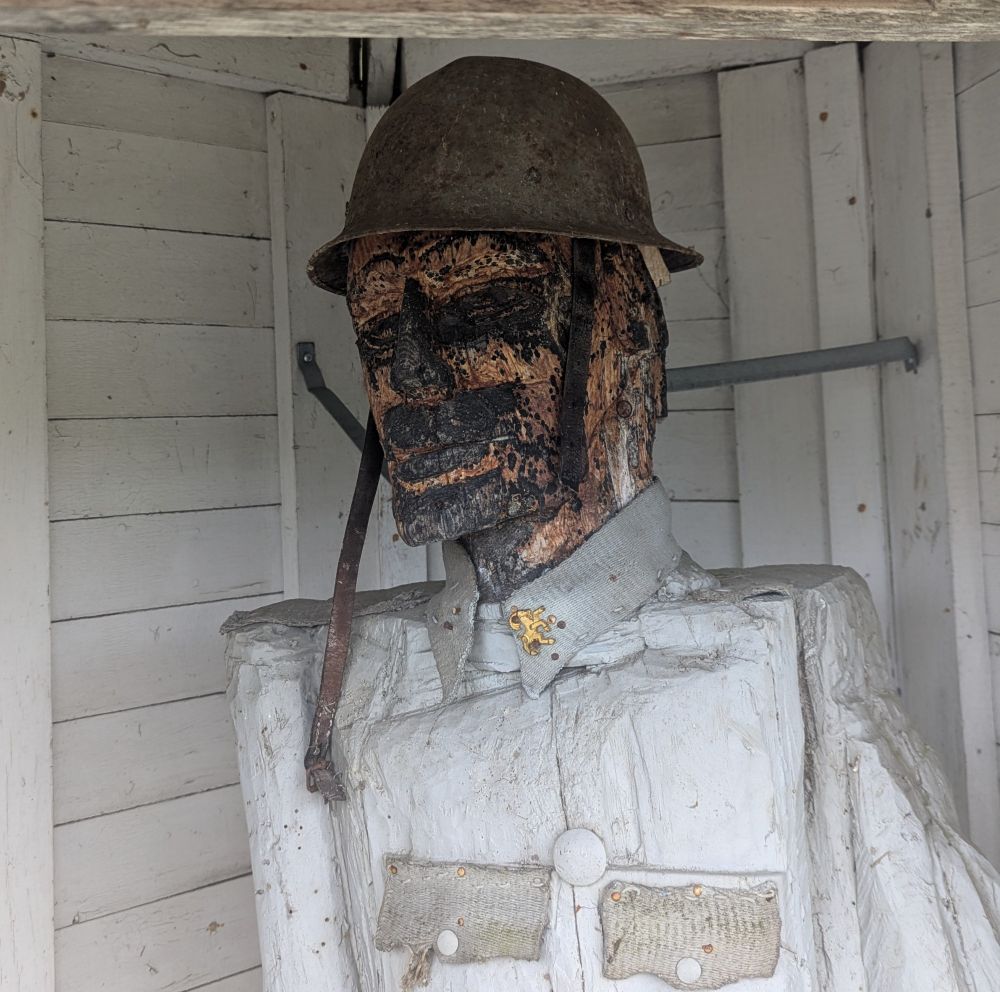 A rotted wooden statue of a Swedish soldier. Its eyes, lips and nose look like they have been burned off, though it is likely just the decaying paint.