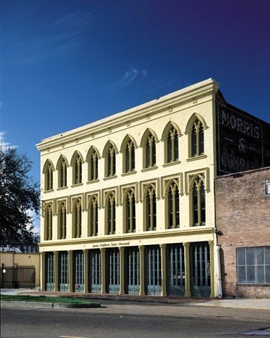 Photograph of a three-story warehouse building with Gothic revival details on the second and third stories, and cast iron columns with wide doors between them on the ground floor