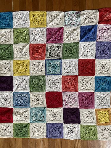 a handknit blanket of alternating multicolored and white squares with a lace motif