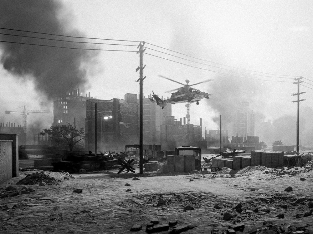 A photograph of a helicopter hovering several meters above the ground in front of several ruined buildings on the New Sobek City map.