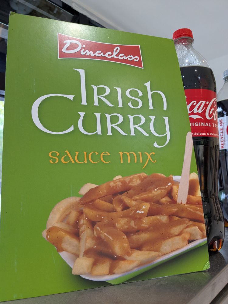 A green sign on the counter of a chip shop, advertising 