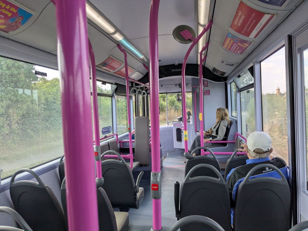 The inside of a largely empty bus, with just two other passengers. The poles are painted pink.