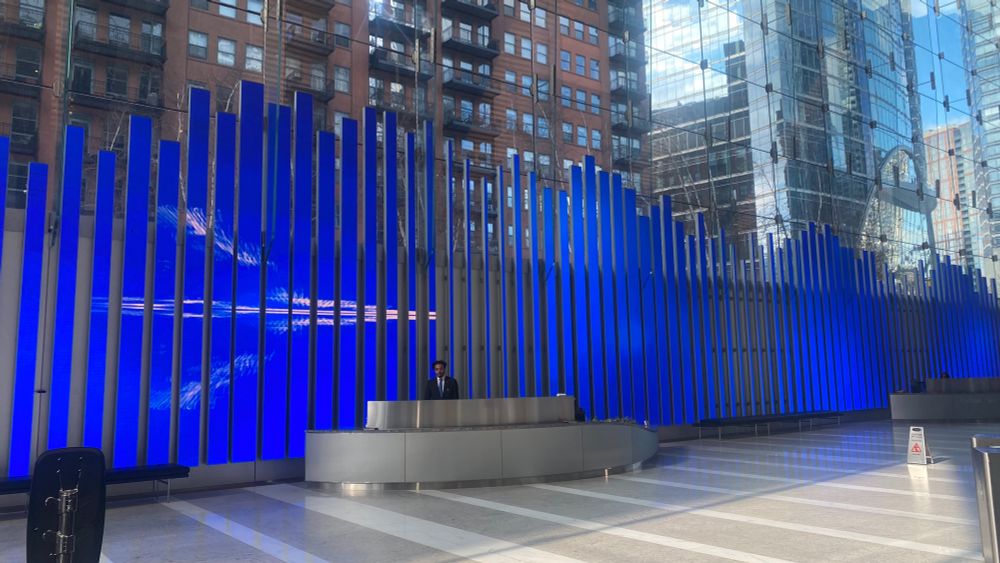 A long slatted led screen in with a white bird like figure against a blue background. A curved metal courtesy desk sits in front of the screen with attendant 