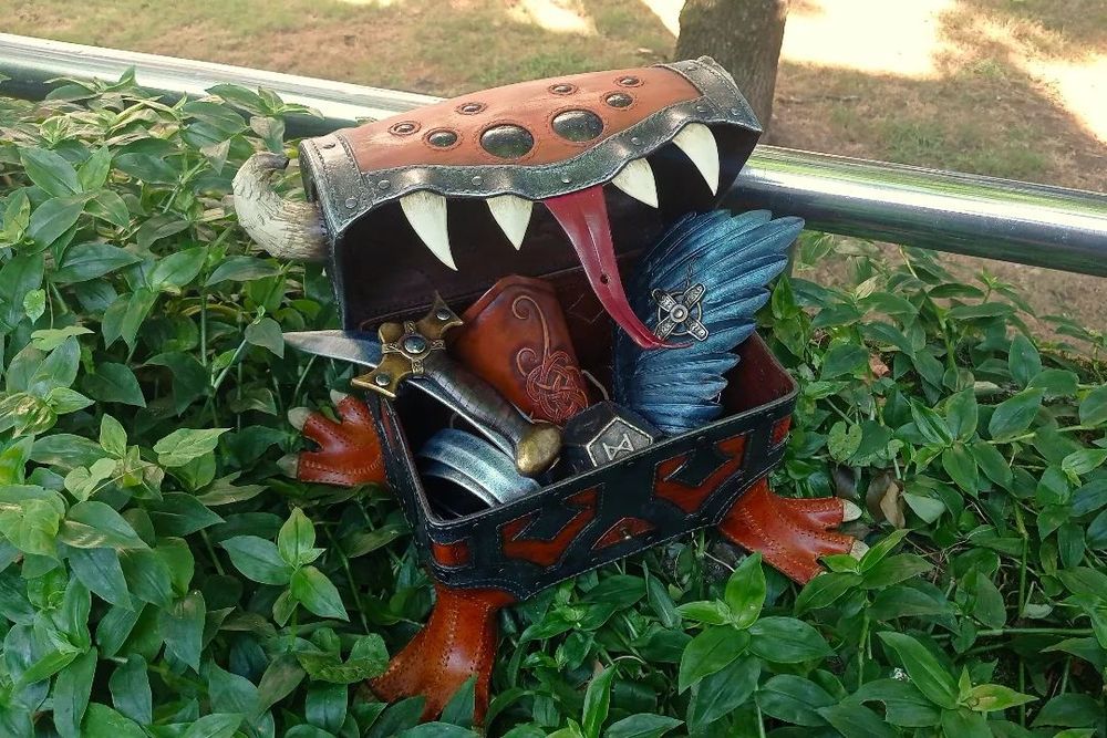 The mimic has its mouth wide open, revealing a variety content: a sword shaped belt, a viking style cuff, a blue wing simulated bracer, a bronze roman polyhedron and a brass cross pendant