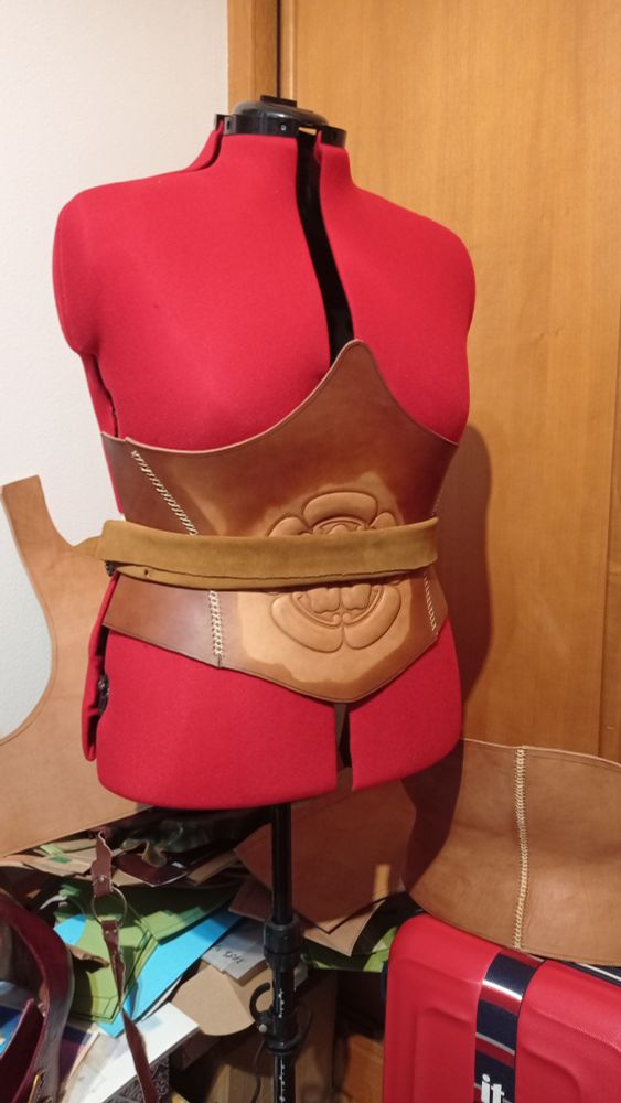 Pic of the front piece of the corset damped (except for the mon embossing) and wrapped around the mannequin waist, secured with a belt and a piece of suede and moulded