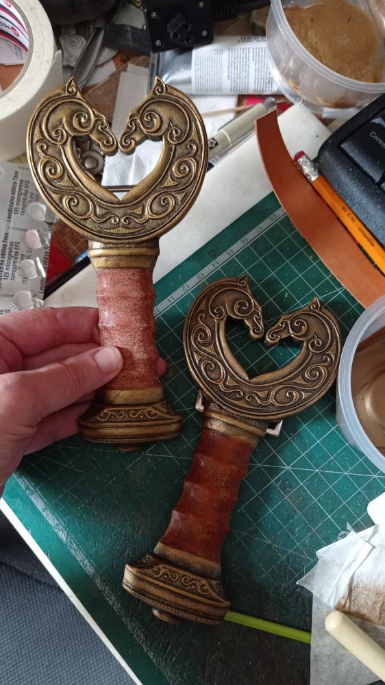 Close pic of the hilt/buckles of the Théoden swordbelts, now the darkest one is much more golden but still having dark contrast accentuating the volumes, and the lightest has the shadows less dark, and the volumes are retouched with light gold acrylic painting