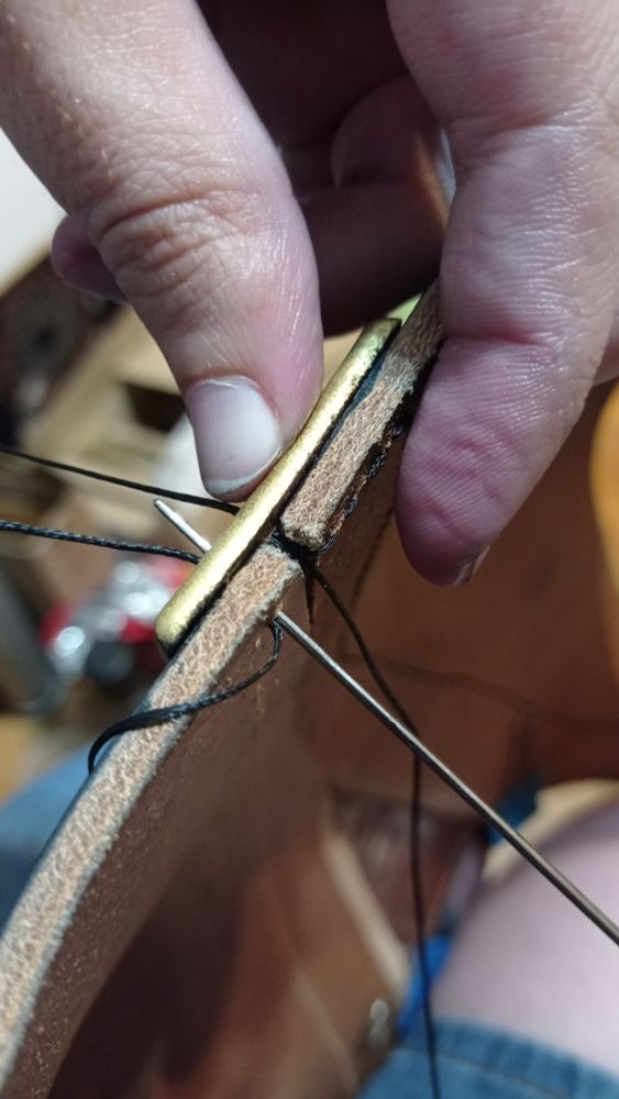 Detail pic of the bottom edge of the center part of the chest pieces, attached together, the needle going through the sewing hole, middle stitch, to show the thickness of the leather the needle is perforating, and my fingers grabbing it all to compare sizes