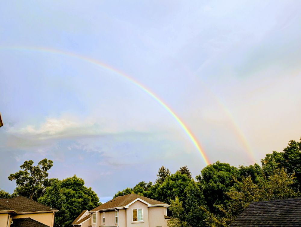 Picture of a double rainbow over houses and trees. 