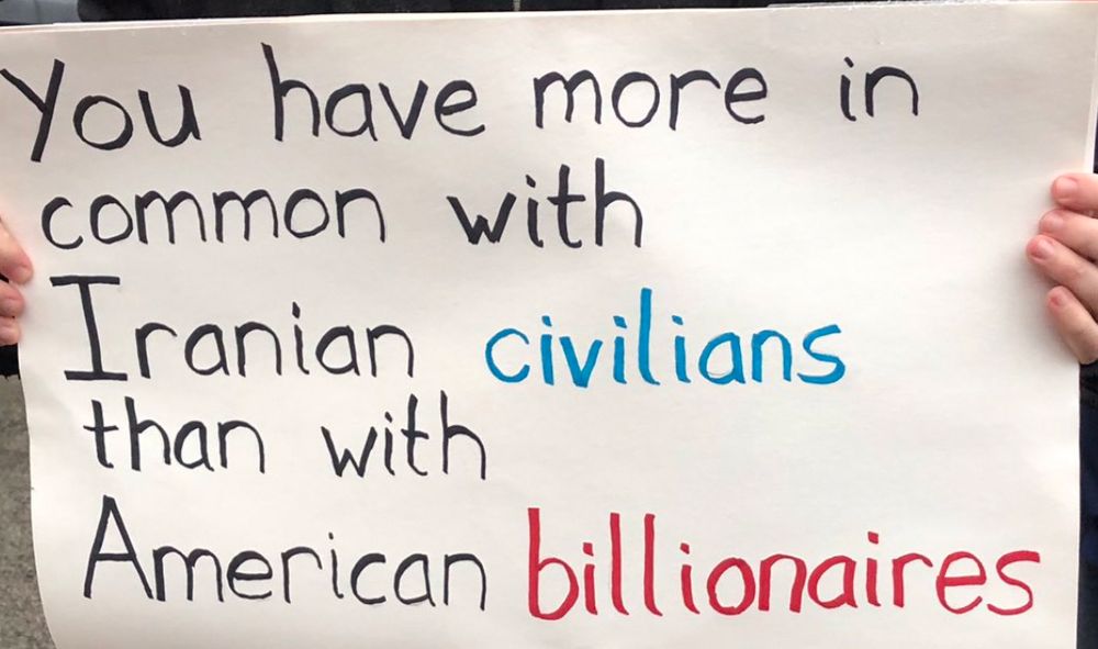 a sign that says “you have more in common with iranian civilians than with american billionaires” — the lettering is in black, “civilians” is in blue & “billionaires” is in red