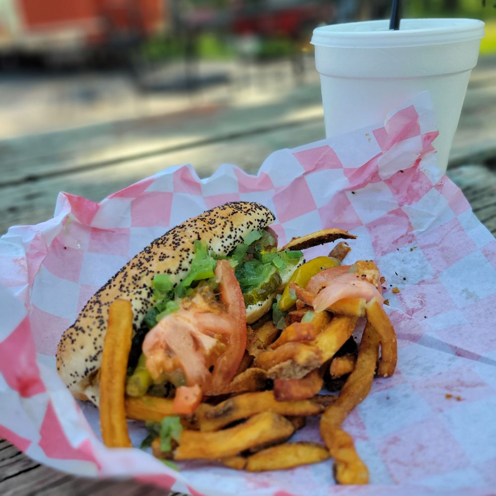 A Chicago dog (no onions!!) with fries and drink on a picnic table. 
