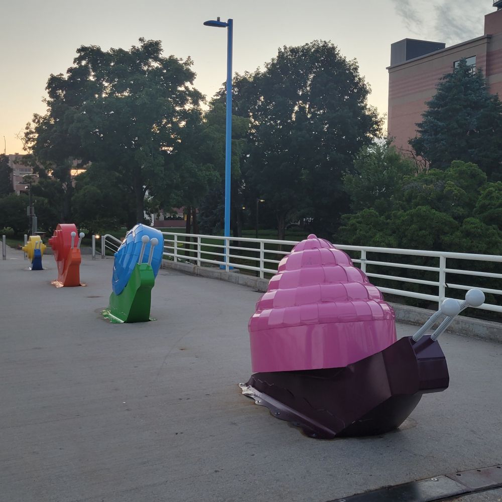 A series of colorful snail sculptures on a pedestrian bridge in the evening.