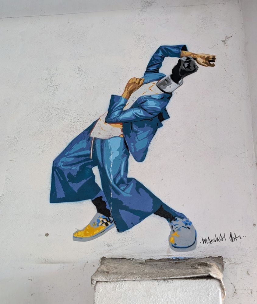 Ein Wesen in einem blauen Anzug in kämpferischer Verrenkung.
Statt des Kopfes ist eine geballte Faust zu sehen.