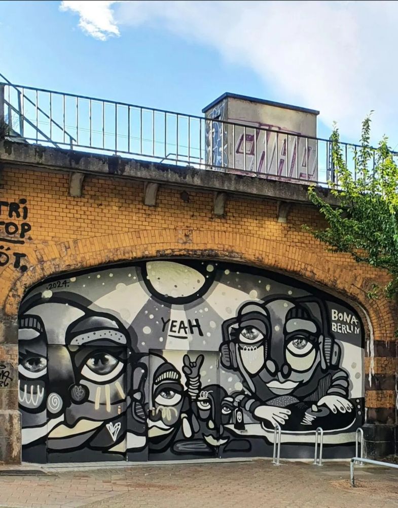 Dieses Mural im Bogen der Deichtor-Kasematten kann bald sein Einjähriges feiern.
In den Abstufungen weiß grau schwarz sind Köpfe dargestellt a la Picasso. Mittig eine Sonne, deren Strahlen das obere Drittel des Szenario ausfüllen.
In der Mitte steht
YEAH.