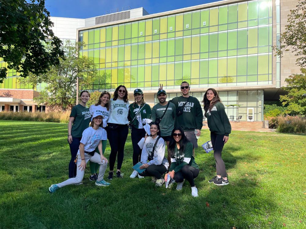 10 people on a green lawn in front of a green building wearing MSU green/white and MI Parkinson Foundation gear. Despite what it looks like my knee was unharmed in the taking of this photo.