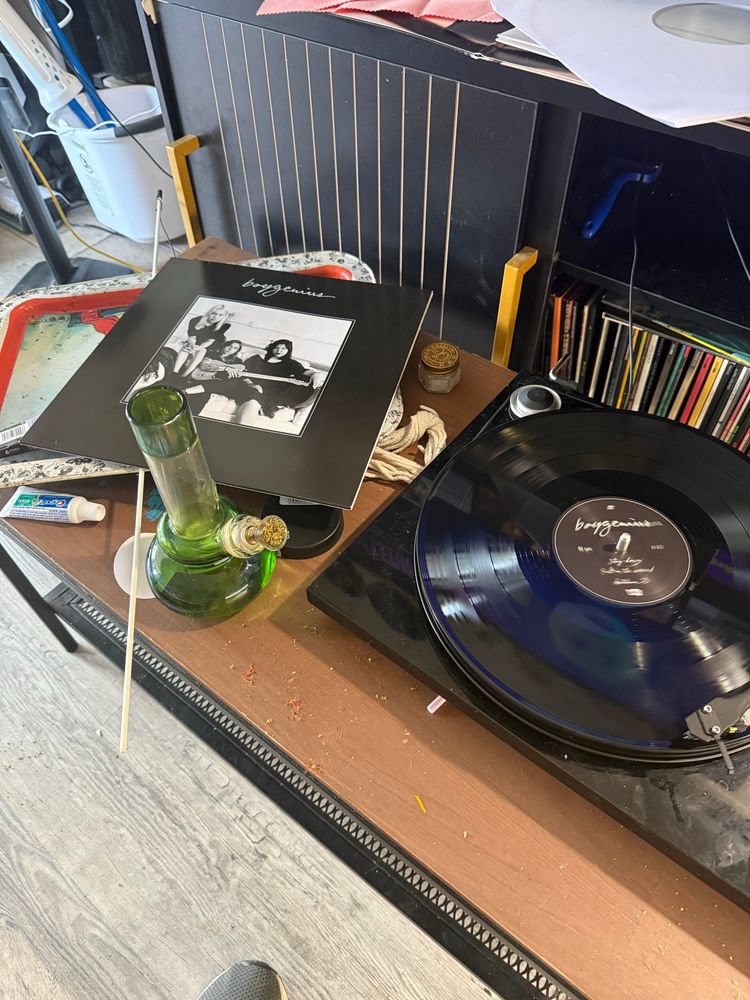 A messy coffee table most prominently holding a packed bong, and boygenius’ the record spinning on a record player 