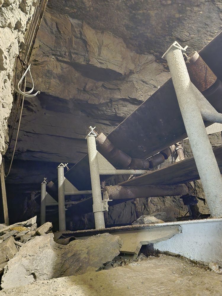 Photo of a conveyor belt emerging from a dark, inclined shaft.