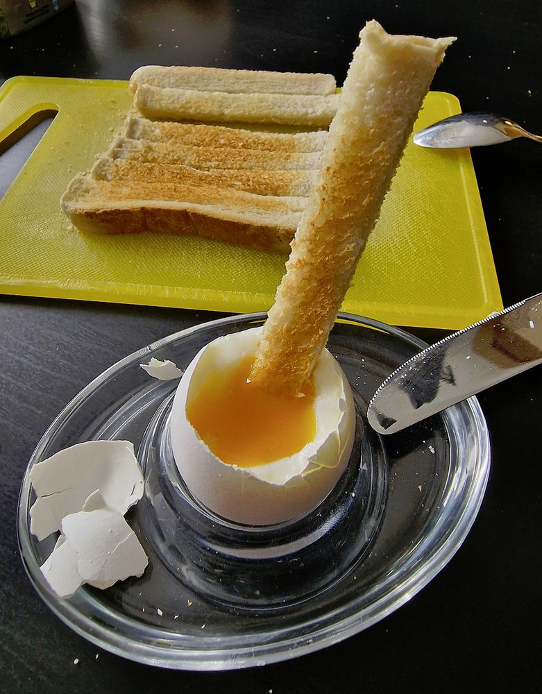 Photo of a soft-boiled egg's yolk being dipped with a strip of toast.