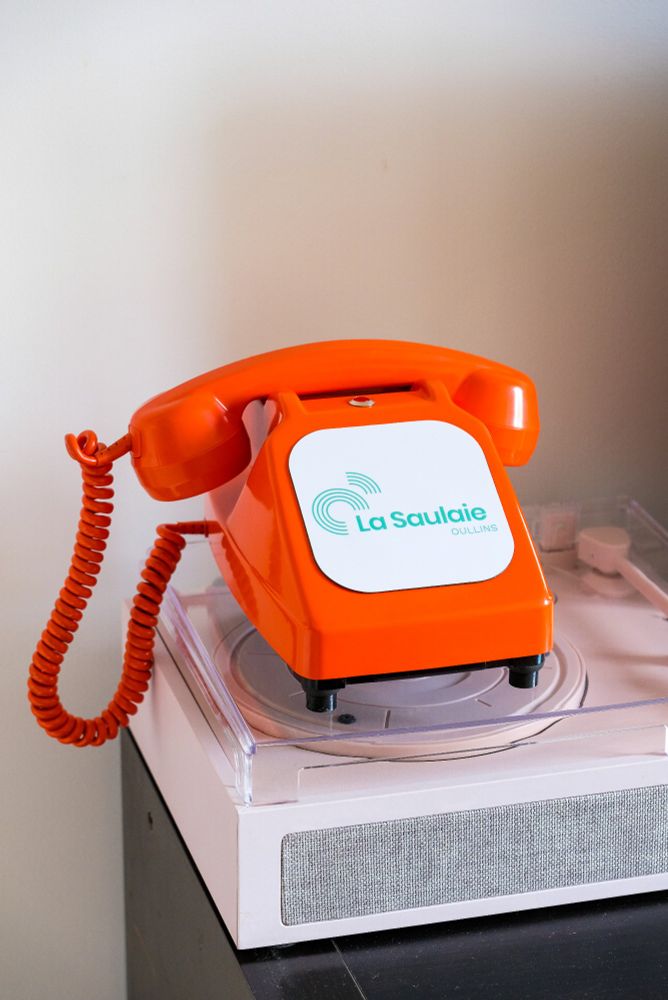 Téléphone orange avec une plaque a la place du cadran, qui indique "la Saulaie, Oullins"