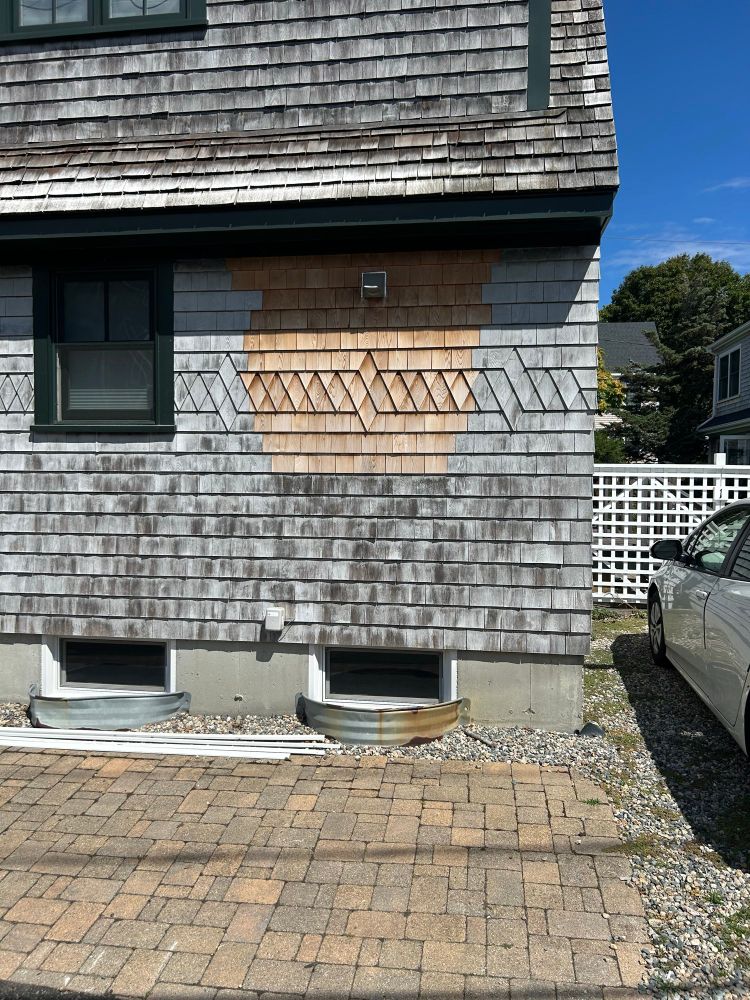 A picture of cedar shake siding on a building. Some of the cedar shakes have been replaced so there is new siding juxtaposed to the weather worn siding. 