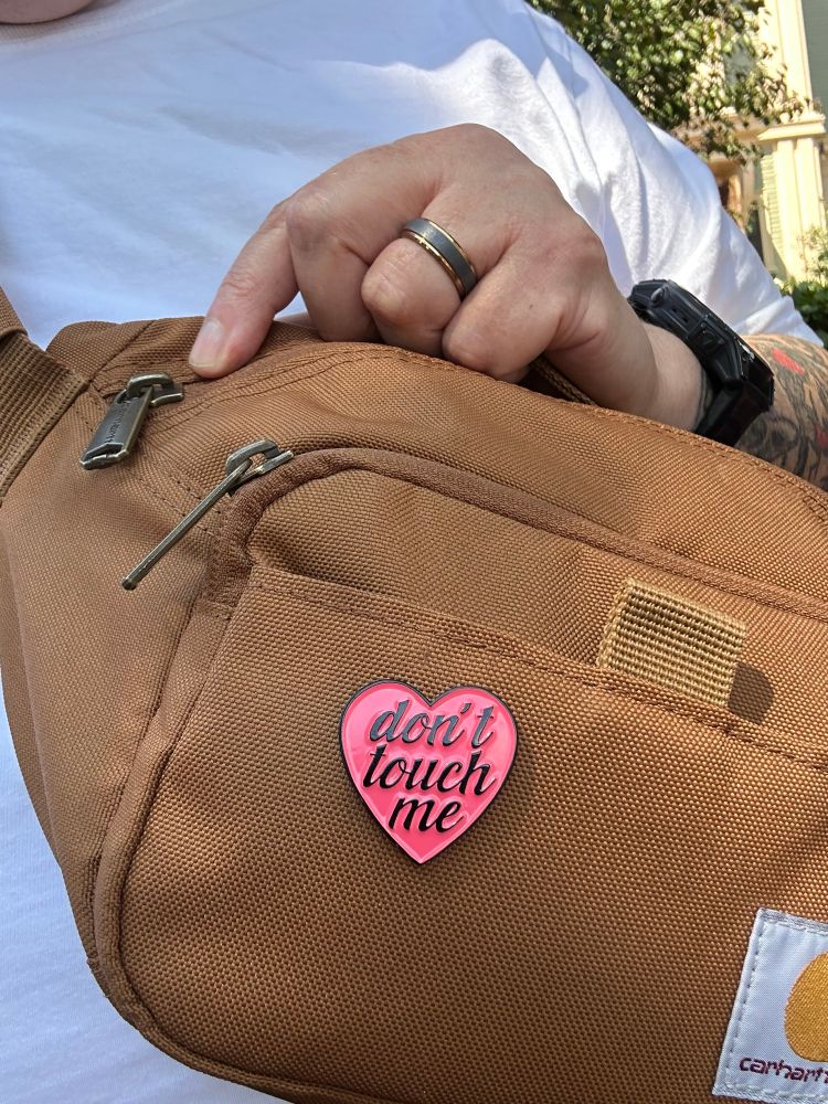 A Carhart cross body bag with a heart pin that reads: don’t touch me 