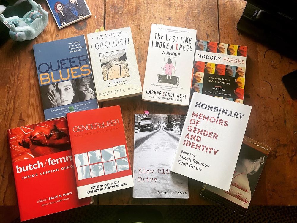 A smattering of books, all laid out on a table. Some are theory, some are fiction, some nonfiction. Pictured here are: Butch/femme Genderqueer Slow Blind Drive Non-binary Memoirs or Gender and Identity Nobody passes Queer Blues The Well of Loneliness 