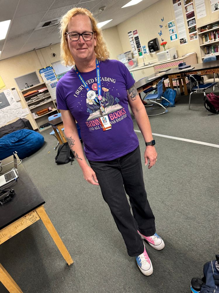A woman with a pronoun pin, Trans pin, and trans flag colored custom Converse. 