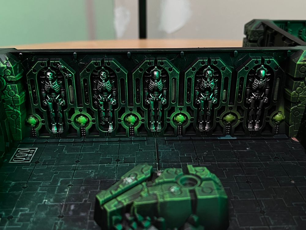 A close-up view of a wall section of the Tomb World board, featuring Necron warriors in various stages of regeneration. 