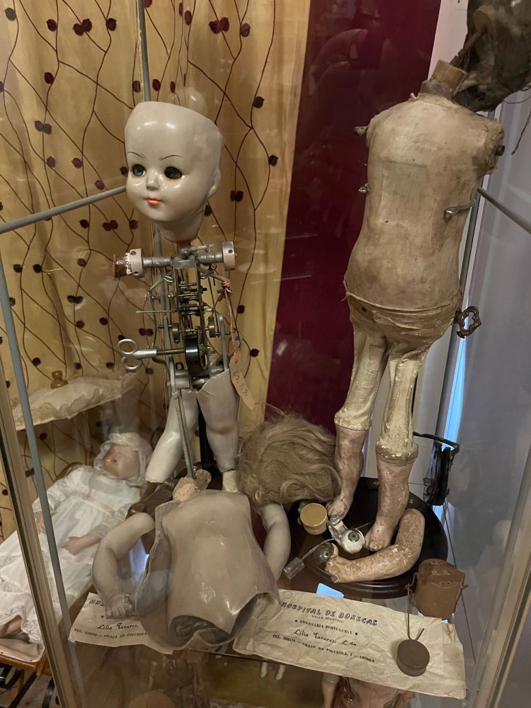 The insides of a mechanical doll with just the face and legs attached, next to a cloth covered doll body with no head 