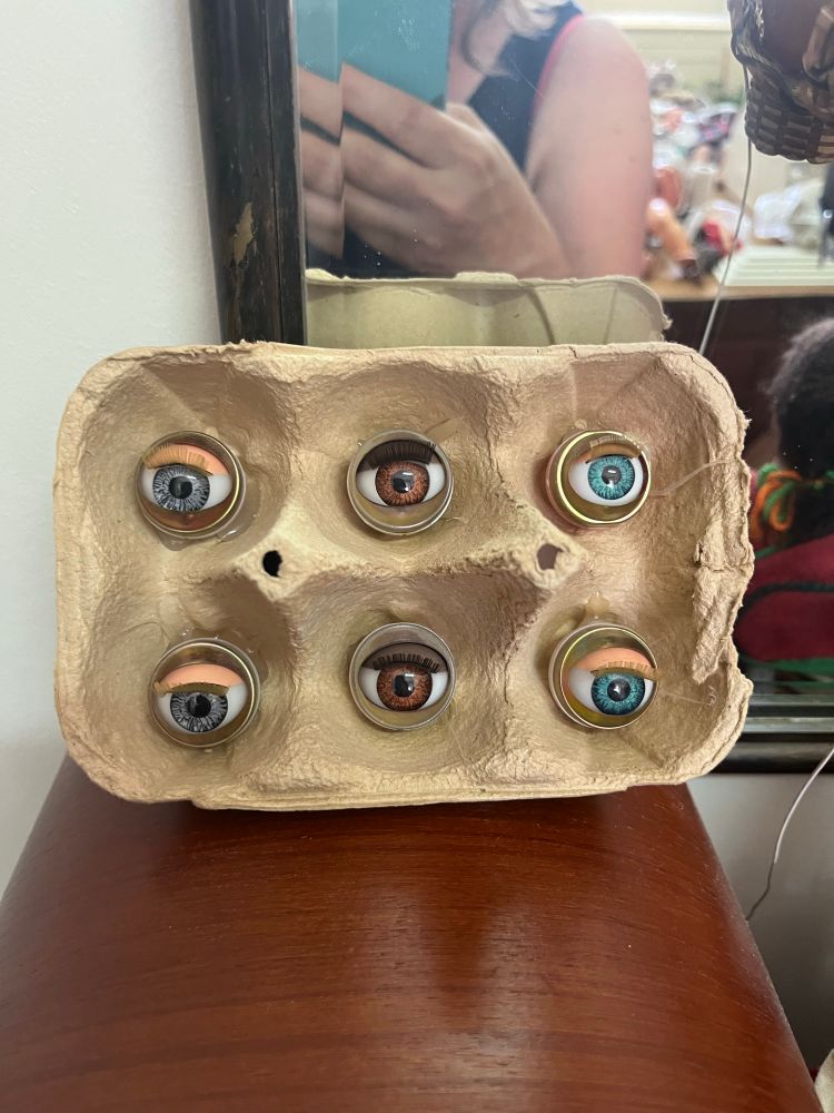 An egg crate with 6 doll eyes instead of eggs