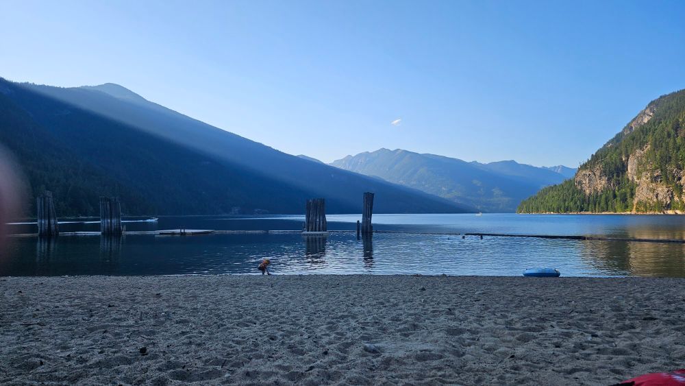 Blue skies, blue water, blue mountains. A picture of a mountain lake beach with pilings sticking out of the water