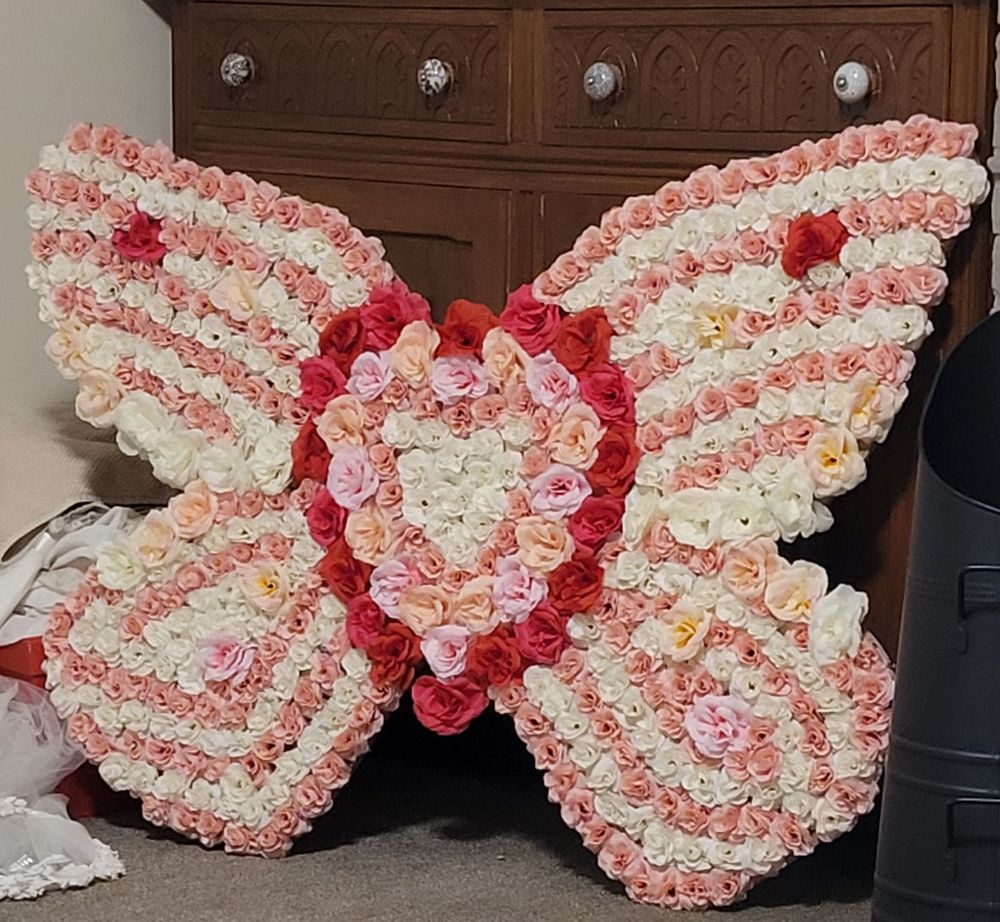 A pink flower tribute in the shape of a butterfly with a red flower heart at the centre.