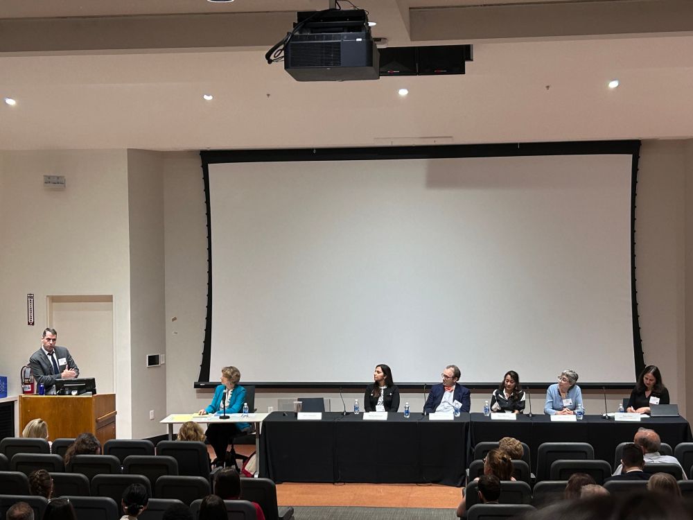 A panel of 7 people of different races and genders sitting at a table 