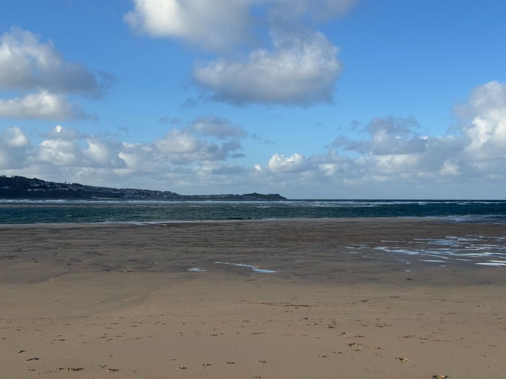 Photo taken from a beach looking across an estuary with St. Ives in the background.