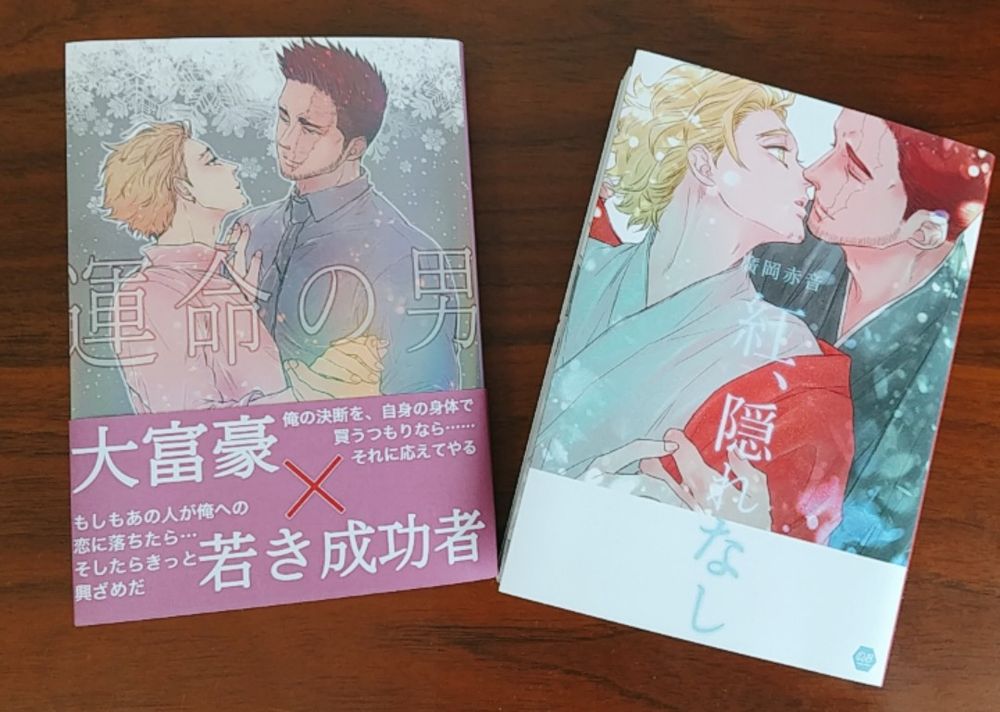 炎ホーの文庫本が2冊並べてテーブルの上に置いてある。「運命の男」フルカラーのカバーにえんじとホが向かい合ってダンスの手を組みあっている姿が描かれ、「大富豪×若き成功者」と大きく書かれた帯が巻いてある。ホログラムPPで一部虹色の光がさしている。「紅、隠れなし」フルカラーのカバーに和装のえんじが、紅の羽織をまとう和装のホを後ろから抱きしめるようにキスしかかっている姿が描かれている。ベルベットPPでしっとりしたマットな色合い。