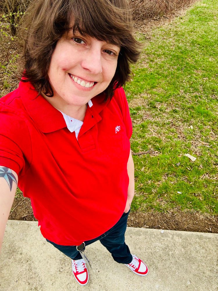 Laura smiling at the camera wearing a short sleeve polo, jeans, and matching Vans. 
