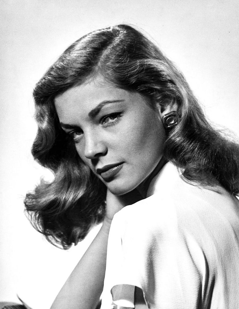 Lauren in a head and shoulders portrait, she’s wearing a white dress and is looking over her left shoulder toward the viewer